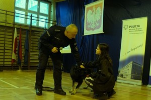 Zdjęcie przedstawia policjanta z psem służbowym oraz jedną z uczennic