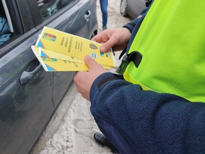 Zdjęcie przedstawia policjanta trzymającego w ręce informacyjne broszury